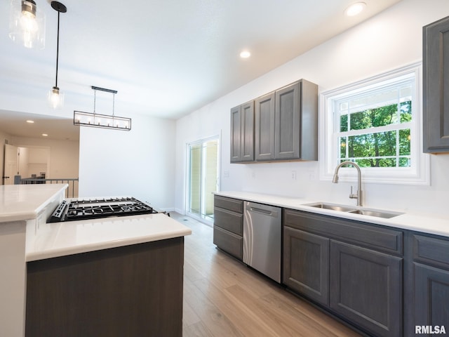 kitchen with stainless steel dishwasher, a sink, gas stovetop, light wood-style flooring, and light countertops