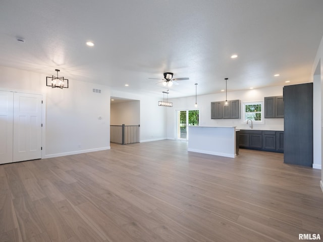 unfurnished living room with a sink, a chandelier, a ceiling fan, light wood finished floors, and recessed lighting
