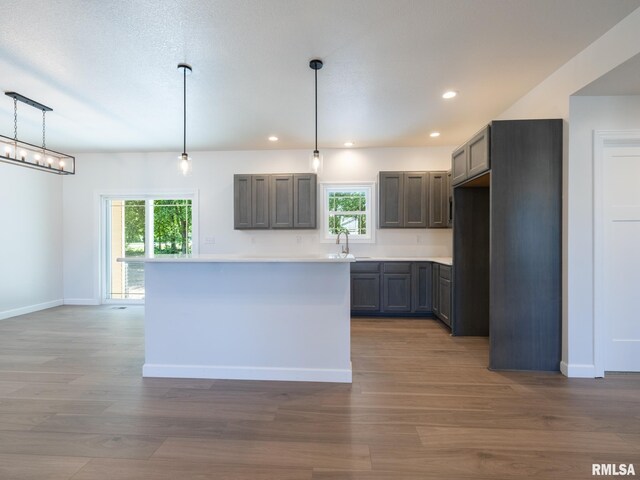 kitchen featuring a sink, wood finished floors, recessed lighting, light countertops, and baseboards