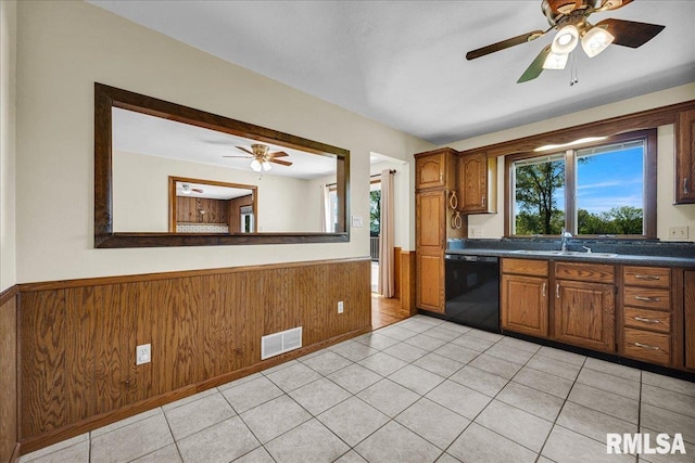 kitchen featuring dishwasher, wainscoting, ceiling fan, a sink, and wooden walls