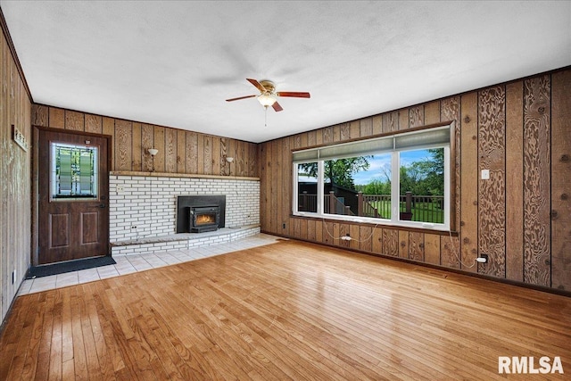 unfurnished living room featuring light wood-style floors, a ceiling fan, wood walls, and a fireplace