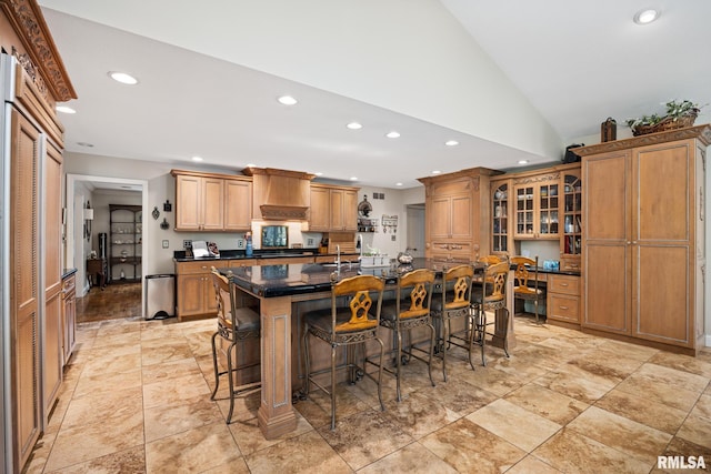 kitchen with recessed lighting, a breakfast bar, a kitchen island with sink, glass insert cabinets, and lofted ceiling