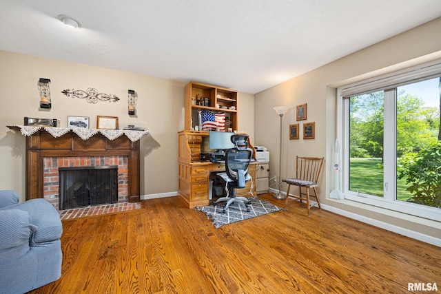 office area featuring wood finished floors, a brick fireplace, and baseboards