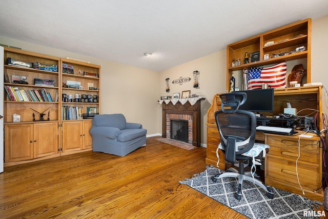 office area with a brick fireplace, wood finished floors, and baseboards