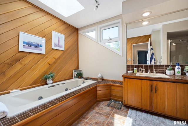 bathroom featuring a skylight, tasteful backsplash, a tub with jets, vanity, and wooden walls