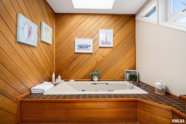 bathroom with a skylight, a jetted tub, and wooden walls