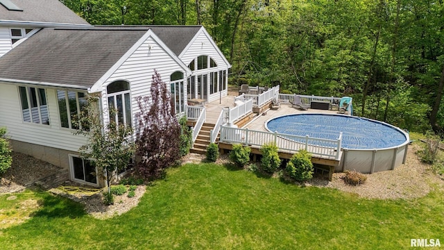 rear view of house with a deck, a covered pool, a yard, and a shingled roof