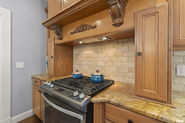 kitchen with stainless steel gas range oven, decorative backsplash, light stone countertops, baseboards, and brown cabinetry