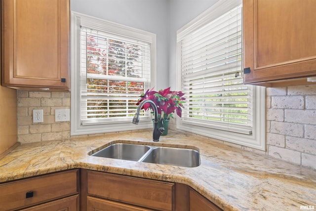 kitchen featuring a sink, healthy amount of natural light, brown cabinetry, and light stone counters