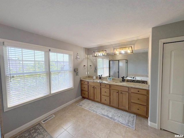 bathroom featuring healthy amount of natural light, double vanity, a stall shower, and tile patterned floors