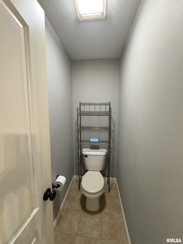 bathroom with toilet, tile patterned floors, a textured ceiling, and baseboards