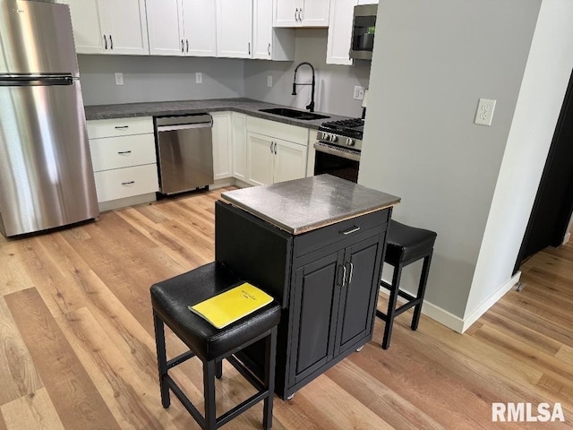 kitchen with appliances with stainless steel finishes, a sink, dark countertops, white cabinetry, and light wood-style flooring
