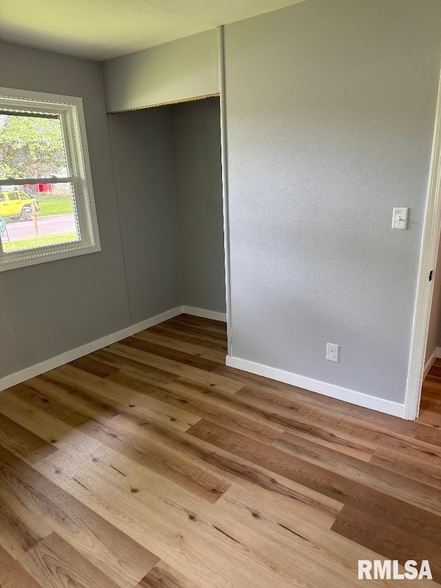 unfurnished bedroom featuring baseboards, wood finished floors, and a closet