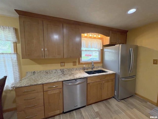 kitchen with stainless steel appliances, a sink, light wood-style flooring, light stone countertops, and recessed lighting