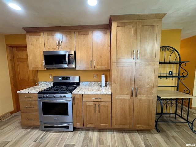 kitchen featuring appliances with stainless steel finishes, light wood finished floors, light stone counters, baseboards, and brown cabinetry