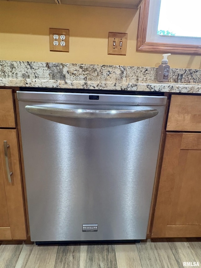 kitchen view of stainless steel dishwasher, light wood-style floors, light stone counters, and brown cabinetry