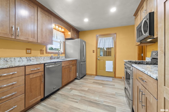 kitchen featuring appliances with stainless steel finishes, a sink, recessed lighting, light stone countertops, and light wood-type flooring