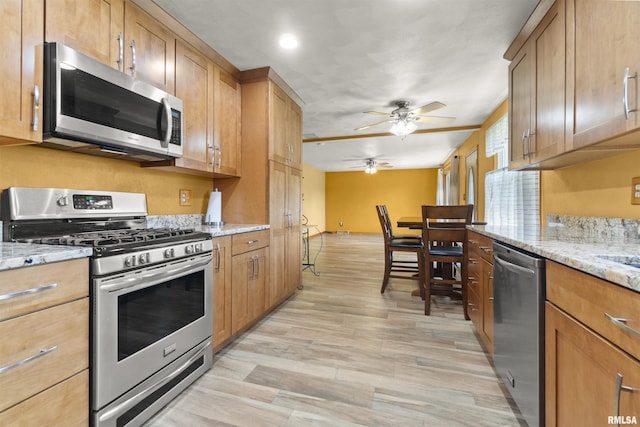 kitchen featuring stainless steel appliances, ceiling fan, light wood-style floors, light stone counters, and brown cabinets