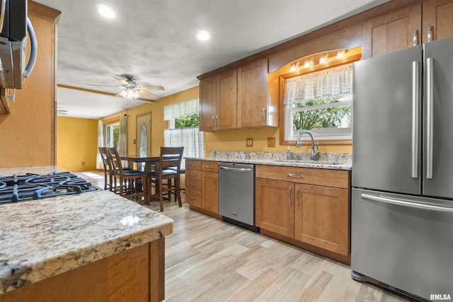 kitchen with stainless steel appliances, a sink, brown cabinetry, light stone counters, and recessed lighting