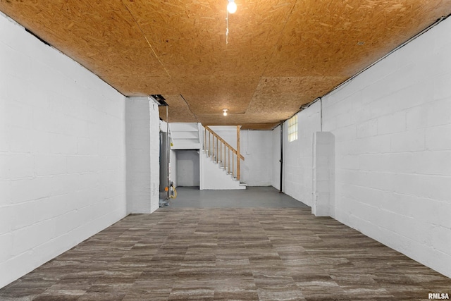 basement with stairs, concrete block wall, and dark wood-style floors