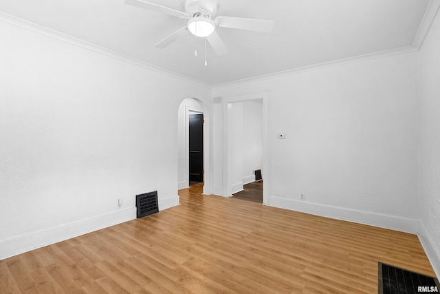 unfurnished room featuring arched walkways, ceiling fan, crown molding, light wood-style flooring, and baseboards