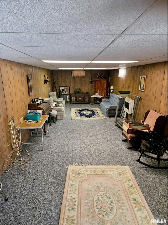 carpeted living area featuring wooden walls and a drop ceiling