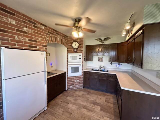 kitchen with white appliances, a sink, dark brown cabinets, ceiling fan, and brick wall
