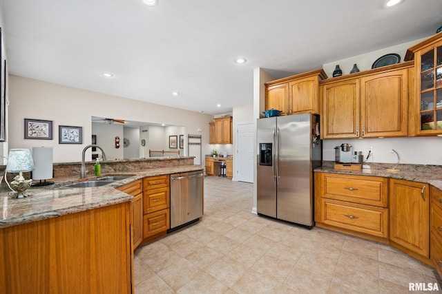 kitchen featuring stainless steel appliances, a sink, glass insert cabinets, stone countertops, and brown cabinets