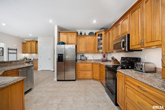 kitchen with appliances with stainless steel finishes, stone countertops, brown cabinetry, glass insert cabinets, and recessed lighting