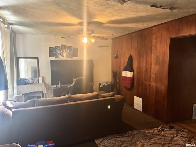carpeted living area featuring ceiling fan, wooden walls, and a textured ceiling