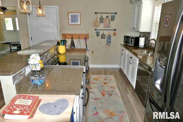 kitchen featuring appliances with stainless steel finishes, wood finished floors, baseboards, a sink, and white cabinetry