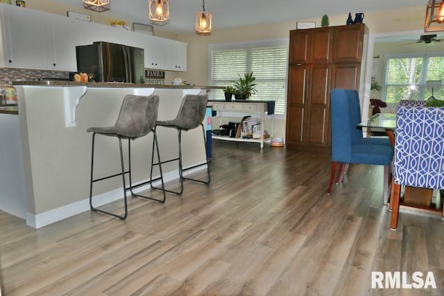 kitchen featuring freestanding refrigerator, a breakfast bar, light wood finished floors, and healthy amount of natural light