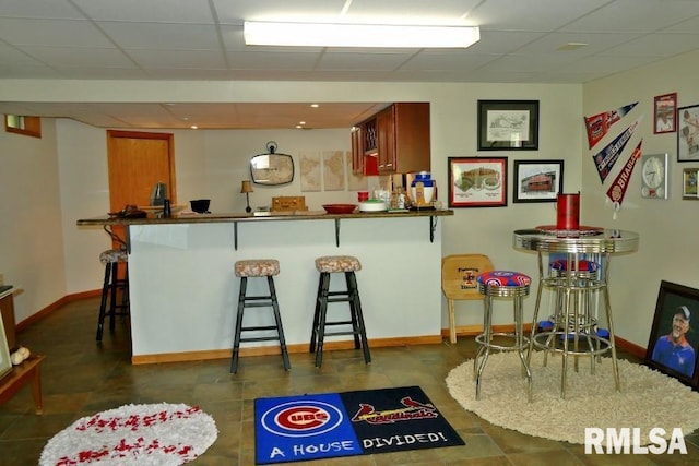 kitchen featuring a drop ceiling, a breakfast bar, baseboards, a peninsula, and dark countertops
