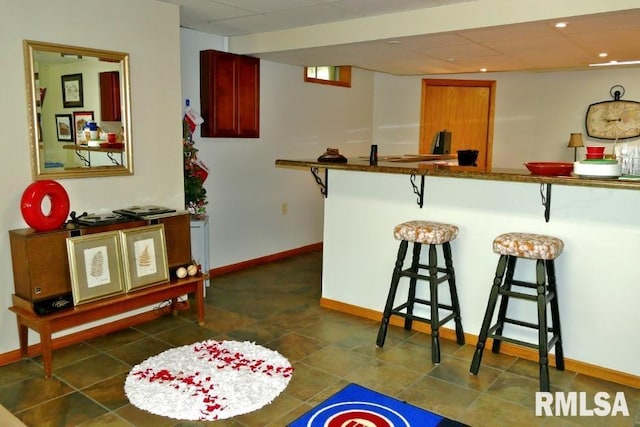 kitchen with a breakfast bar, baseboards, a paneled ceiling, and dark tile patterned flooring