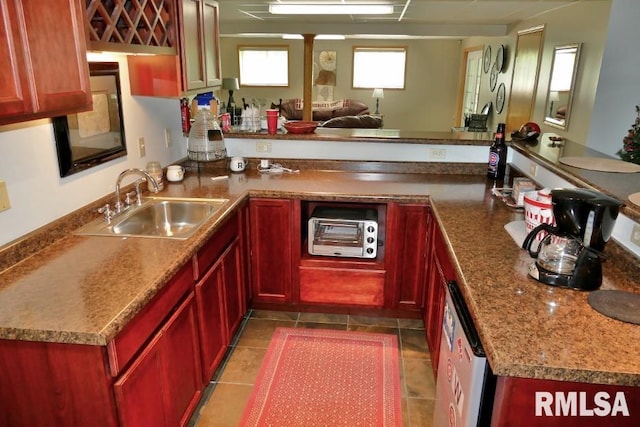 kitchen featuring a sink, reddish brown cabinets, dishwasher, a peninsula, and dark tile patterned floors