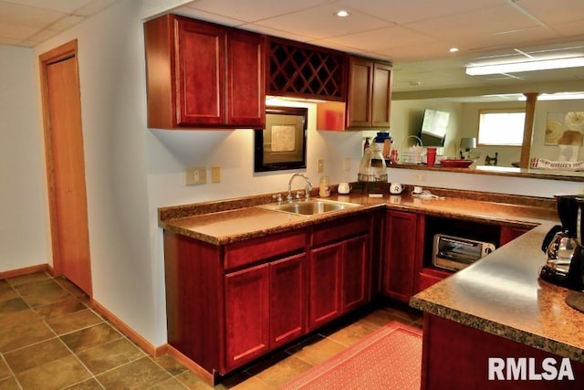 kitchen with reddish brown cabinets, a sink, a drop ceiling, dark countertops, and recessed lighting