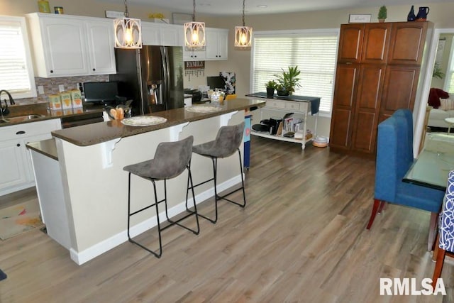 kitchen featuring dark countertops, stainless steel fridge with ice dispenser, light wood-type flooring, a breakfast bar area, and a center island