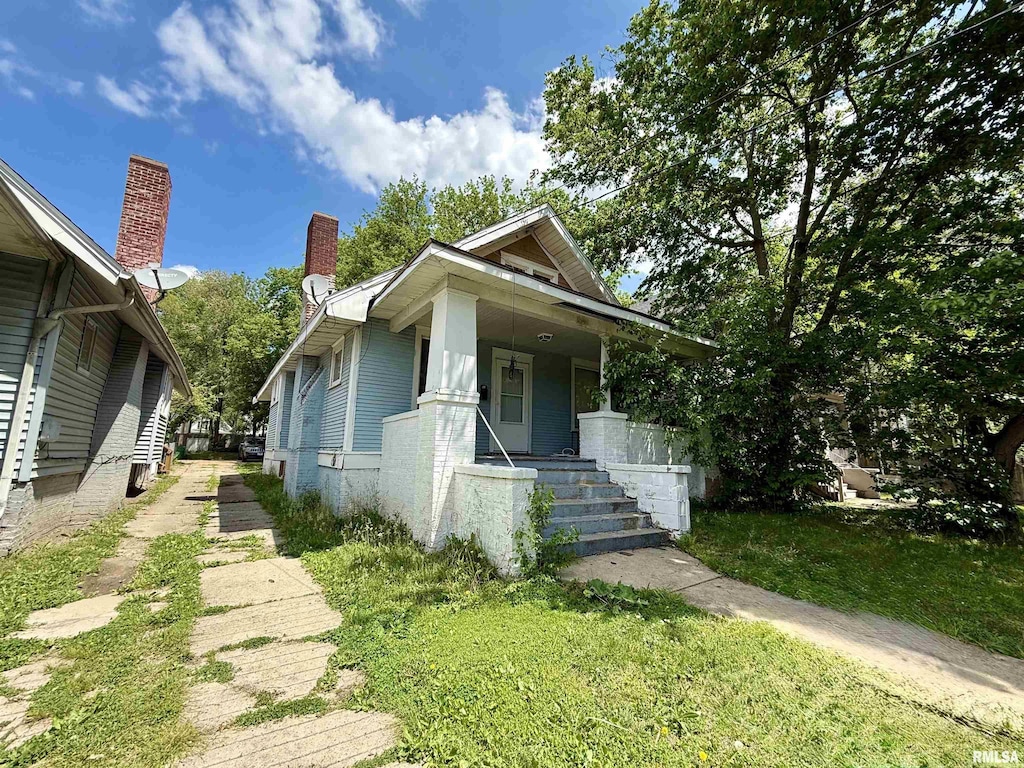 view of front of home featuring covered porch, a chimney, and brick siding