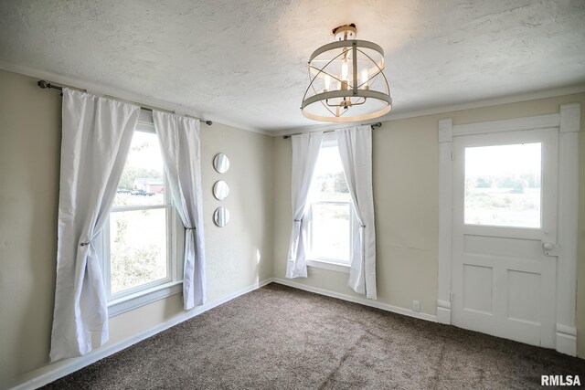 carpeted empty room with a textured ceiling, a chandelier, baseboards, and crown molding