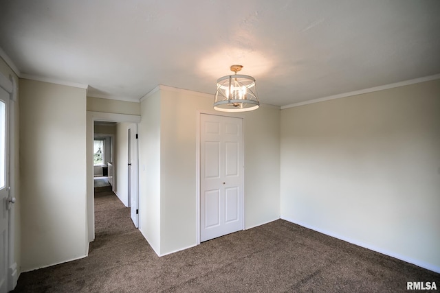 spare room with a chandelier, dark colored carpet, and ornamental molding
