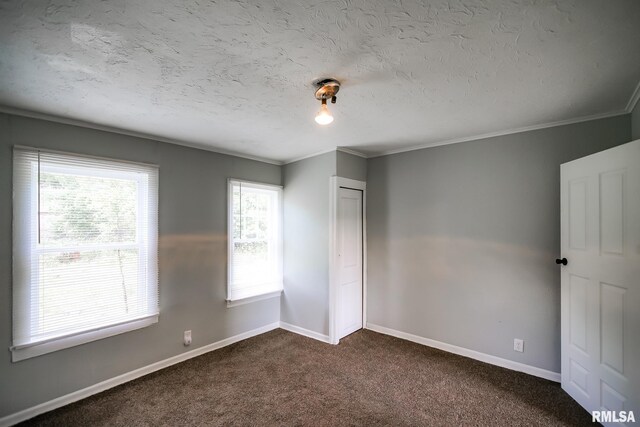 unfurnished bedroom with baseboards, dark carpet, ornamental molding, a textured ceiling, and a closet