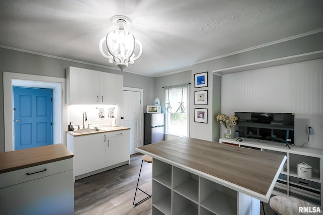 kitchen with butcher block countertops, a sink, a breakfast bar area, ornamental molding, and light wood-style flooring