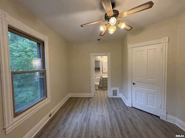 2704 N Dechman Ave, Peoria, IL 61603 - unfurnished bedroom with dark wood-type flooring, baseboards, ensuite bathroom, and a ceiling fan