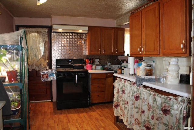 153 S Apple St, Farmington, IL 61531 - kitchen with gas stove, under cabinet range hood, brown cabinets, a textured ceiling, and crown molding