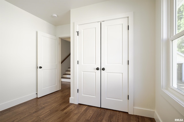 unfurnished bedroom with dark wood-style floors, baseboards, and a closet
