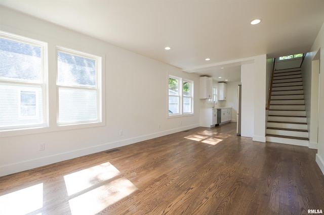 unfurnished living room featuring stairs, dark wood-style floors, baseboards, recessed lighting, and a sink