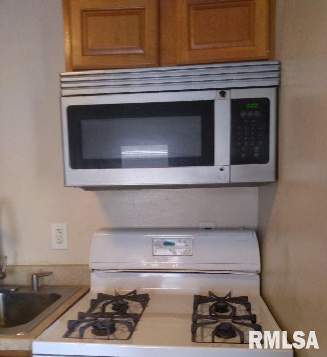 129 Pierson St, East Peoria, IL 61611 - kitchen view of white range with gas stovetop, stainless steel microwave, brown cabinets, and light countertops