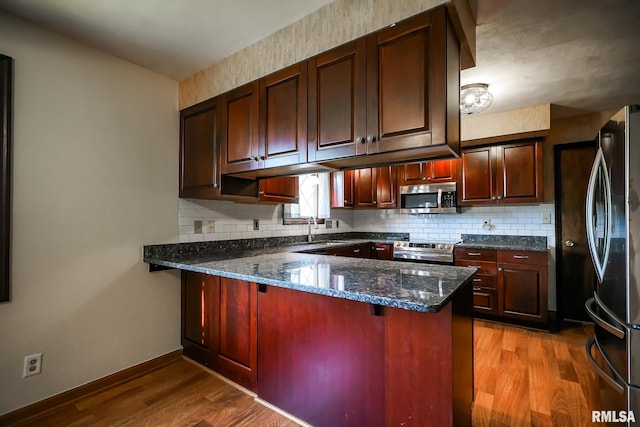 1529 W Richmar Rd, Peoria, IL 61615 - kitchen with stainless steel appliances, a peninsula, wood finished floors, backsplash, and dark stone counters