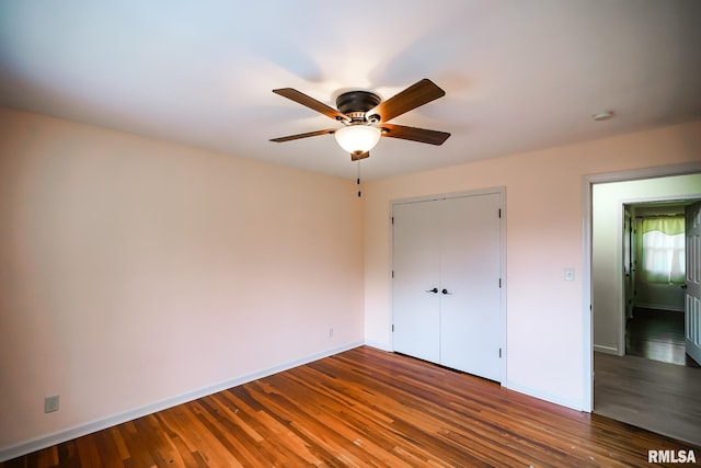 unfurnished bedroom with baseboards, wood finished floors, a closet, and a ceiling fan