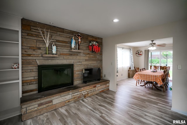 living room featuring wood finished floors, a stone fireplace, baseboards, ceiling fan, and recessed lighting